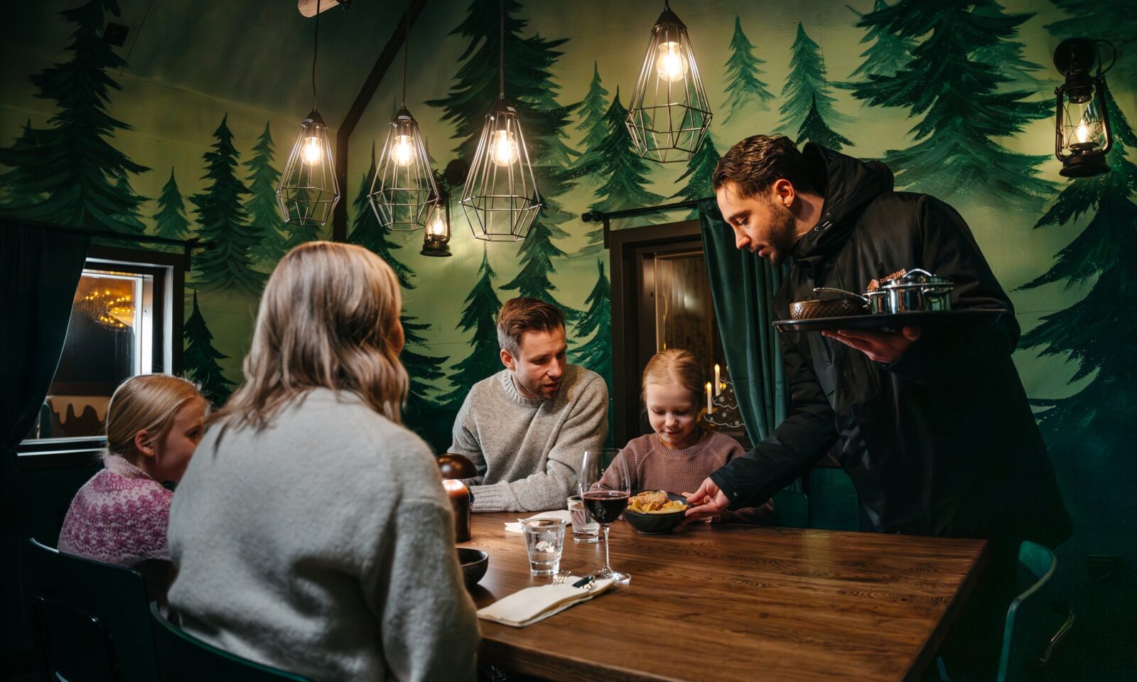 A waiter serving a family in the gingerbread cabin.