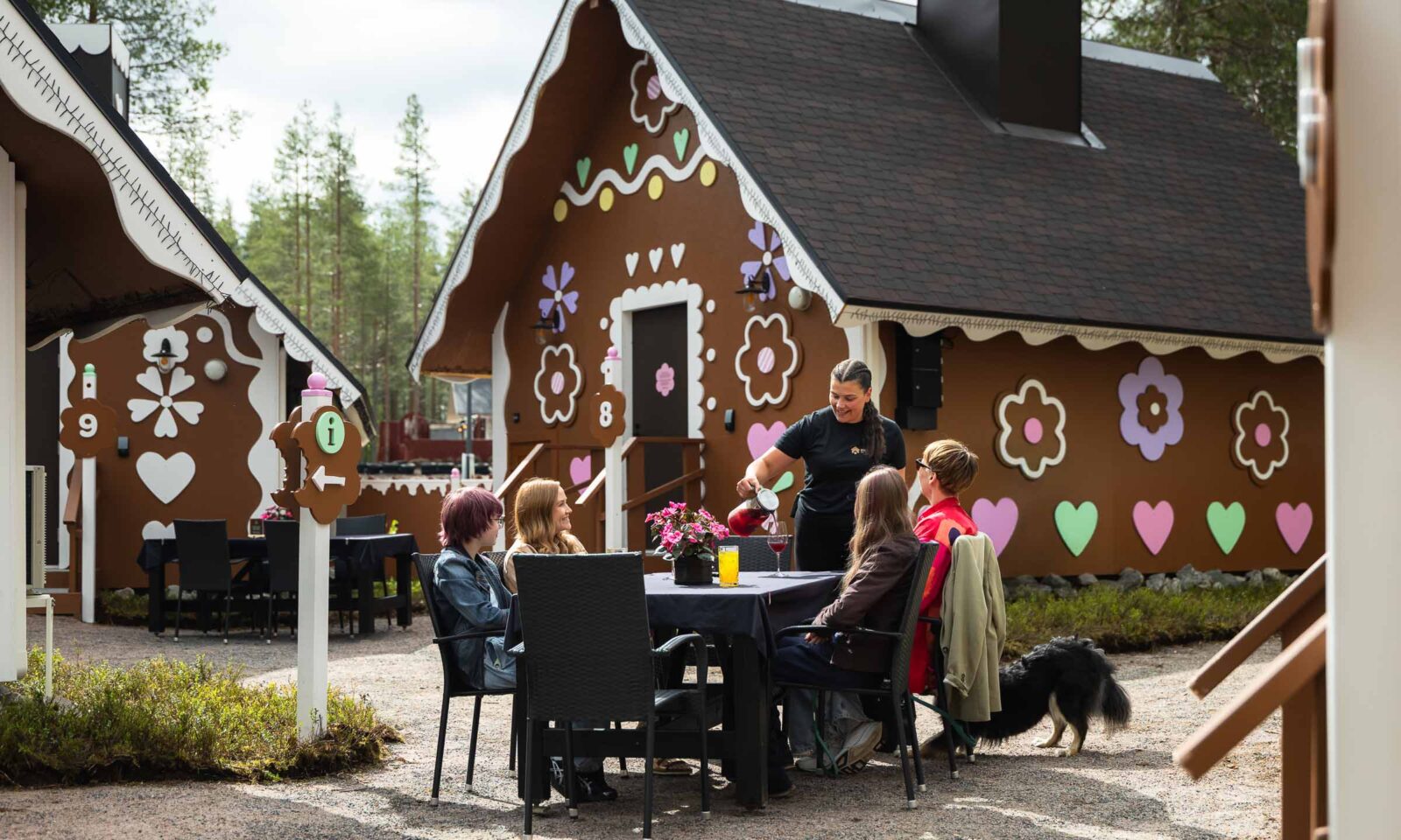Ystäväporukka Piparinan pihalla Joulupukin Pajakylässä Rovaniemellä. Tarjoilija tarjoilee juotavaa.